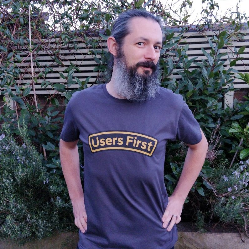 A bearded gentleman wearing a t-shirt which says "Users First". 