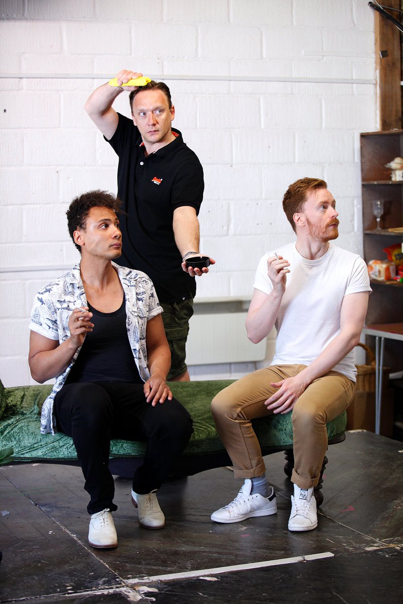 Three men looking surprised. Two of them are sat on a chaise longue. The other is standing.