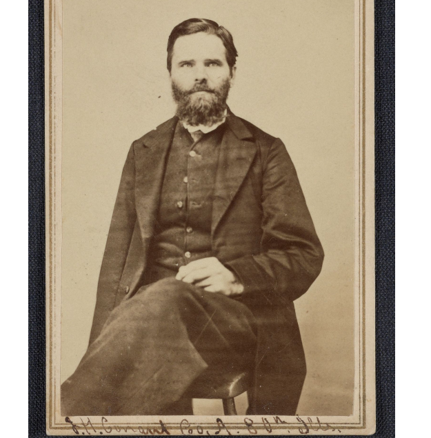 Union Soldier Conant seated. His right arm was amputated after battle. He looks ahead, his left hand rests in his lap. His clothes are worn.