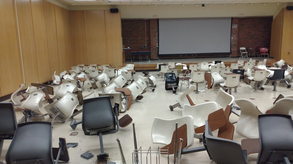 A bunch of chair desks ripped from the floor and lying strewn about
