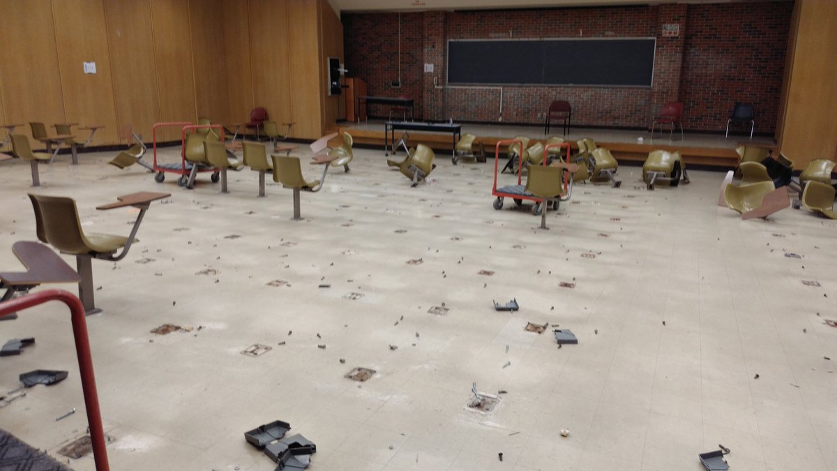 A similar lecture hall with chair desks ripped from the floor, though most are missing