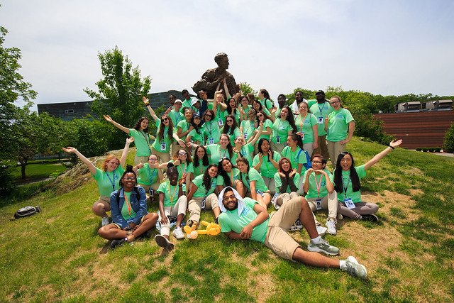large group of students in green t-shirts pose in front of Louis Brandeis statue