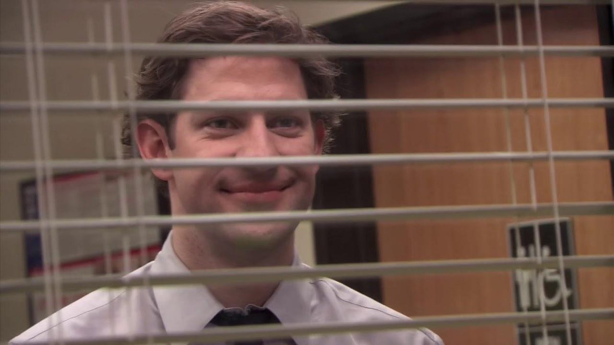 Jim Halpert smiling through blinds, from The Office