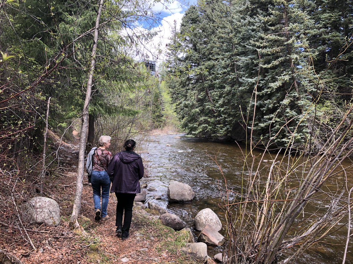 Two physicists (Ana and Priya) walking in front of me along a trail next to a river with trees around