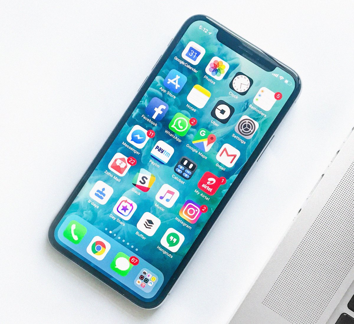 A smartphone next to a laptop, with the screen on and the apps menu in view