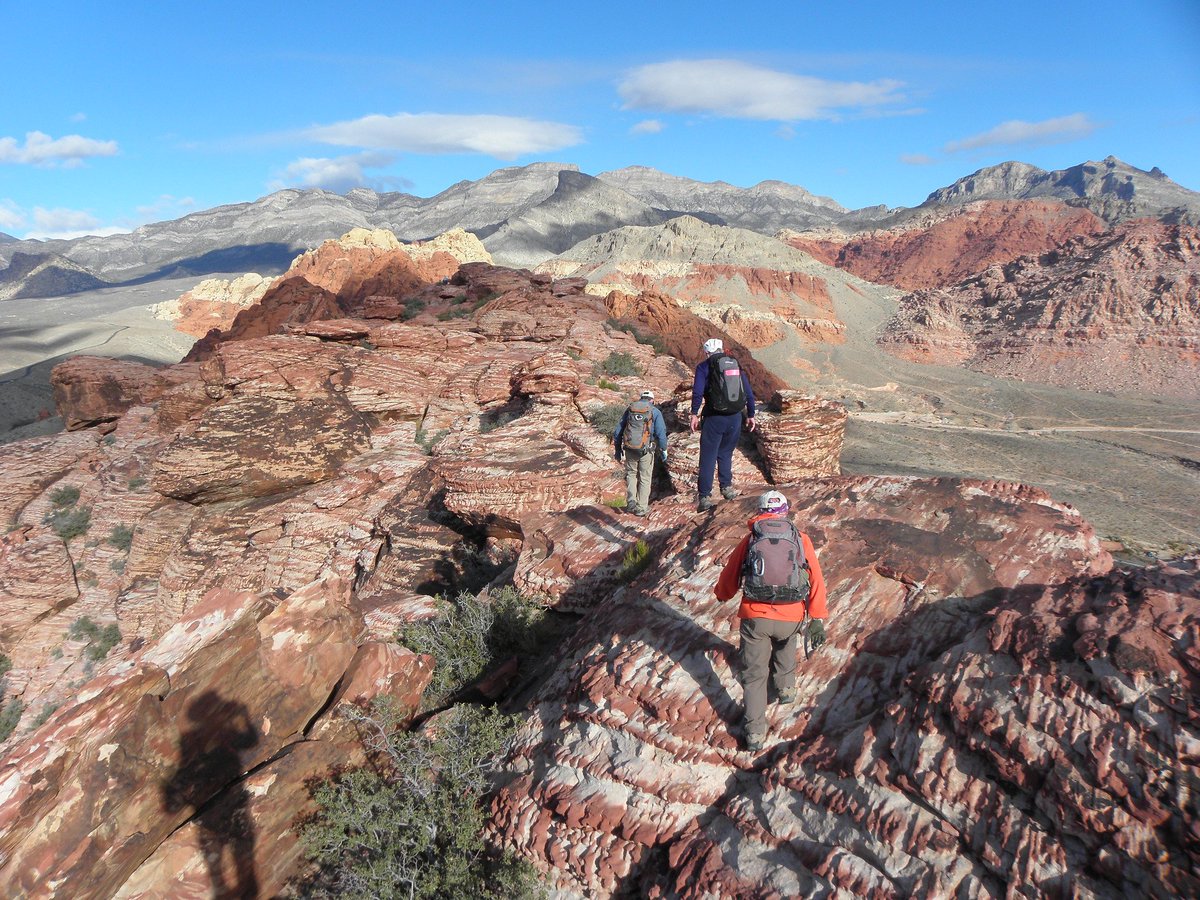 Three men in outdoor gear hike across a landscape of red and white striped rocky hills.