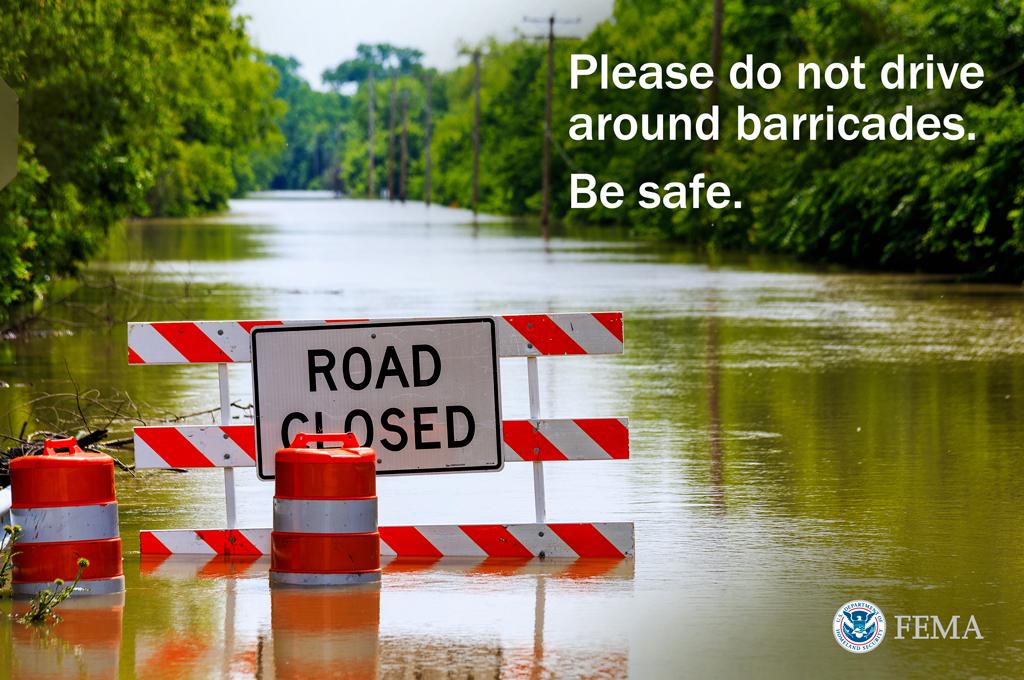 A photo of a flooded road with a barricade and a Road Closed sign.