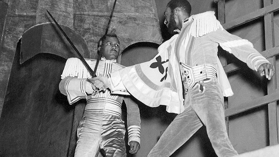 Two swordsmen battling it out on a stage. One definitely does not look enthused.