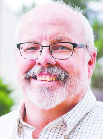 Tom Sullivan, an older man with black-fram glasses, smiles at the camera.