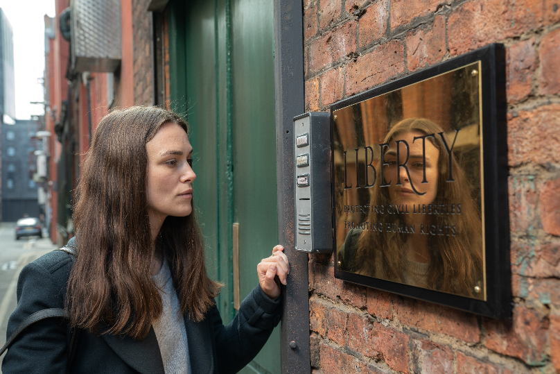 Keira Knightley stands outside a building looking at the intercom in a still from her new film, Official Secrets