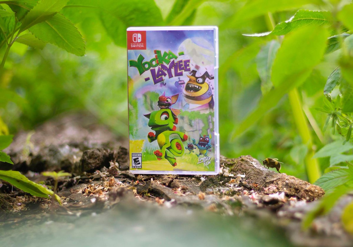 A physical edition of Yooka-Laylee sitting in some soil, surrounded by leaves and a single bee!