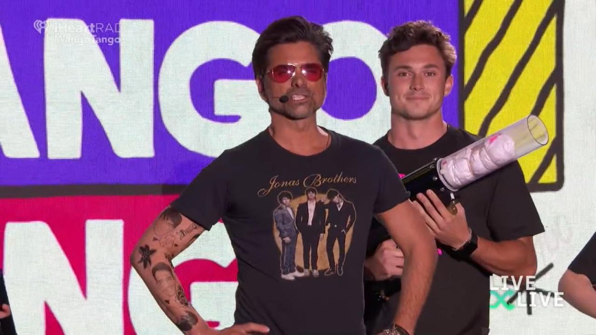 jbrosnews's tweet photo. John Stamos just presented the @JonasBrothers at the #WangoTango! He threw JB t-shirts to the crowd and showed two brand tattoos of Joe and Kevin’s face! https://t.co/ctSgL5KRqN