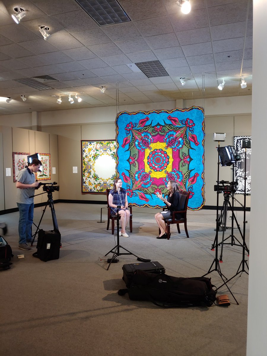 Education Director, Becky Glasby, talks about museum programs in an interview in the gallery. Quilt in center is 'Sedona Rose' by artist Sharon Schamber. For information on museum programs, go to quiltmuseum.org.