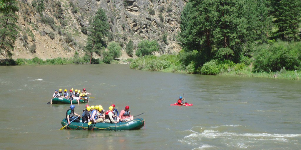 Two inflatable rafts, each holding ten people wearing life jackets and helmets, and one kayaker float down the Salmon River