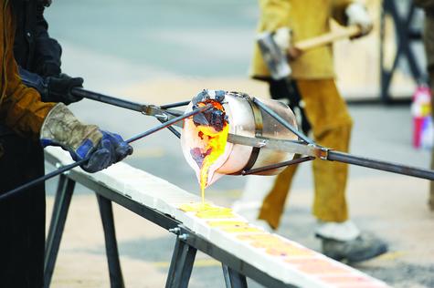 A crucible (small container for heating items) is being tipped to pour molten iron into a long row of small mould blocks.