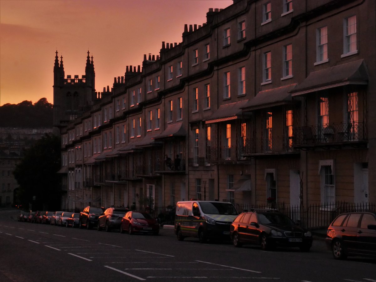 Orange light reflecting in windows of an elegant terrace with a church tower in the background.