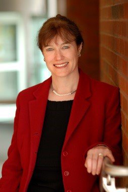 Person wearing black shirt and red jacket stands against a brick wall.