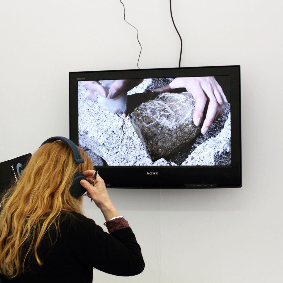 Tv showing film with rocks. A women watches wearing headphones