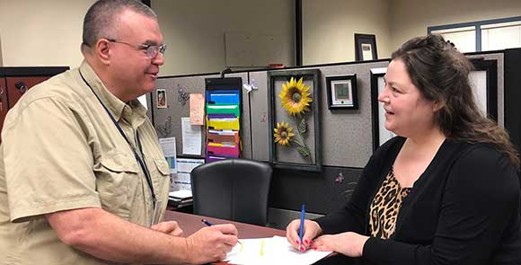 Un homme et une femme discutent debout à un comptoir sur lequel il y a des papiers.