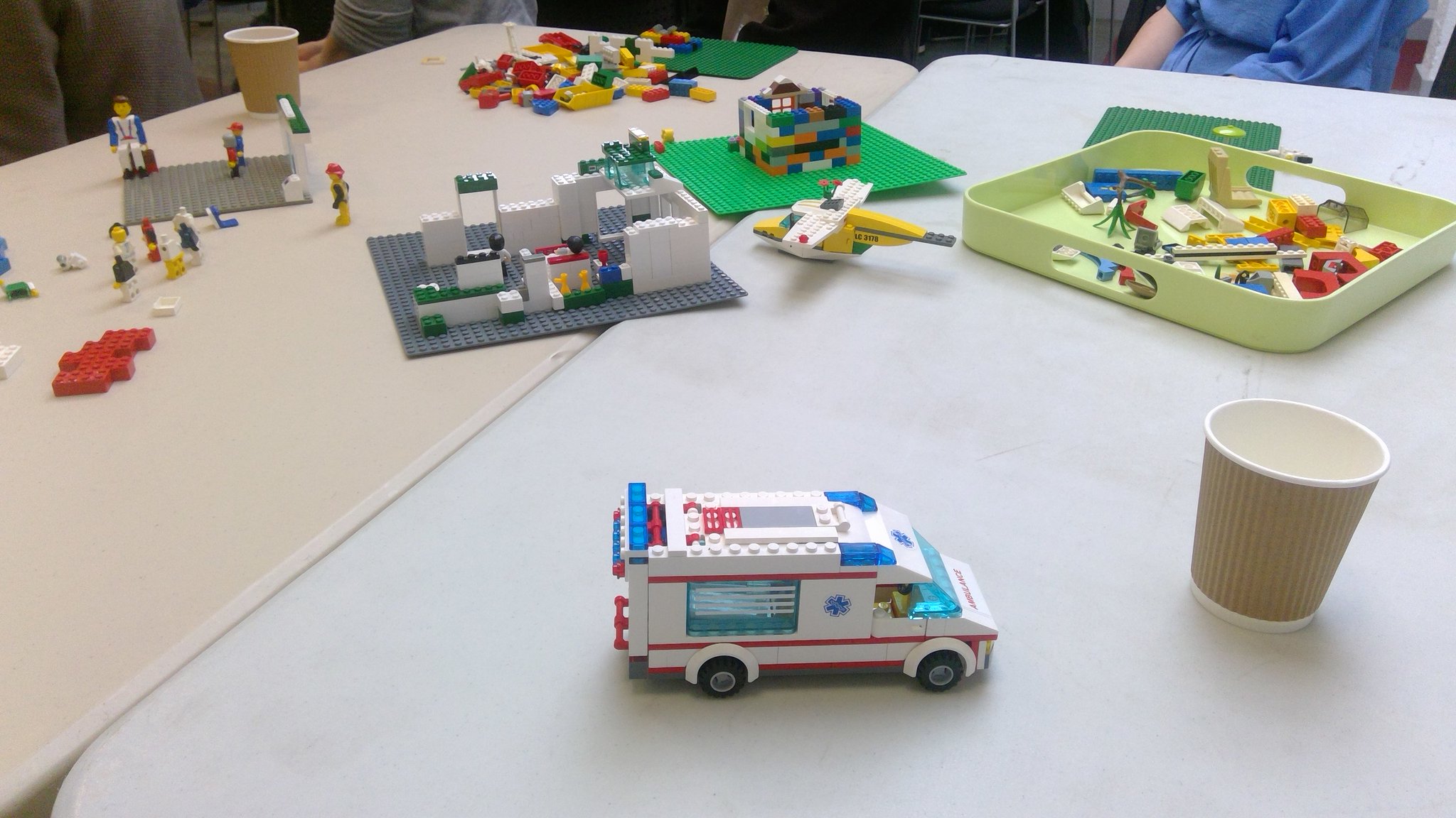 Photograph of a table with a selection of LEGO pieces, including an Ambulance, Helicopter and beginnings of building some rooms.