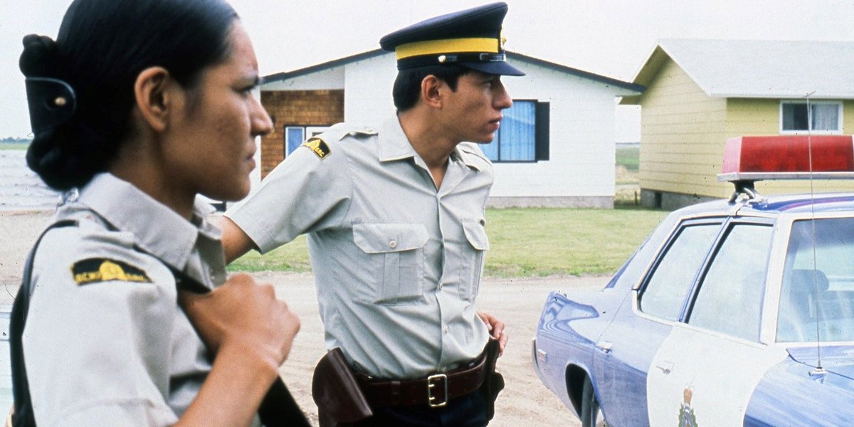 Deux officiers de police autochtones debout à côté d'une voiture de patrouille.