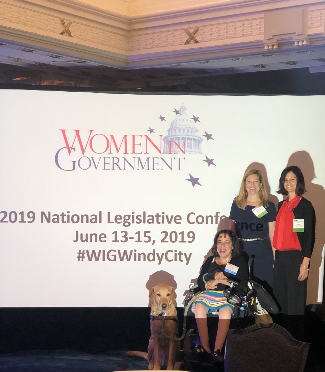 3 women and one service dog in front of white screen with Women in Government written on it