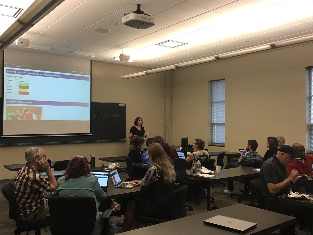 Caryn Pagel leads the group of about 20 people at AccessU 2017 in a team design exercise: Examine this web page, find the accessibility challenges, and offer beautiful solutions!