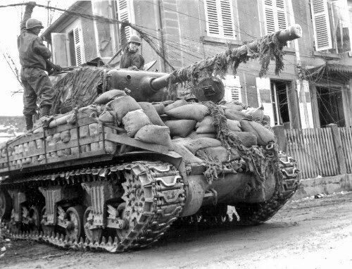 WW2Facts's tweet photo. The crew of a Sherman M4 from the 14th Armored Division drive through a wired connection in #Rittershoffen, France, in March, 1945. https://t.co/fXhYyAxBY4