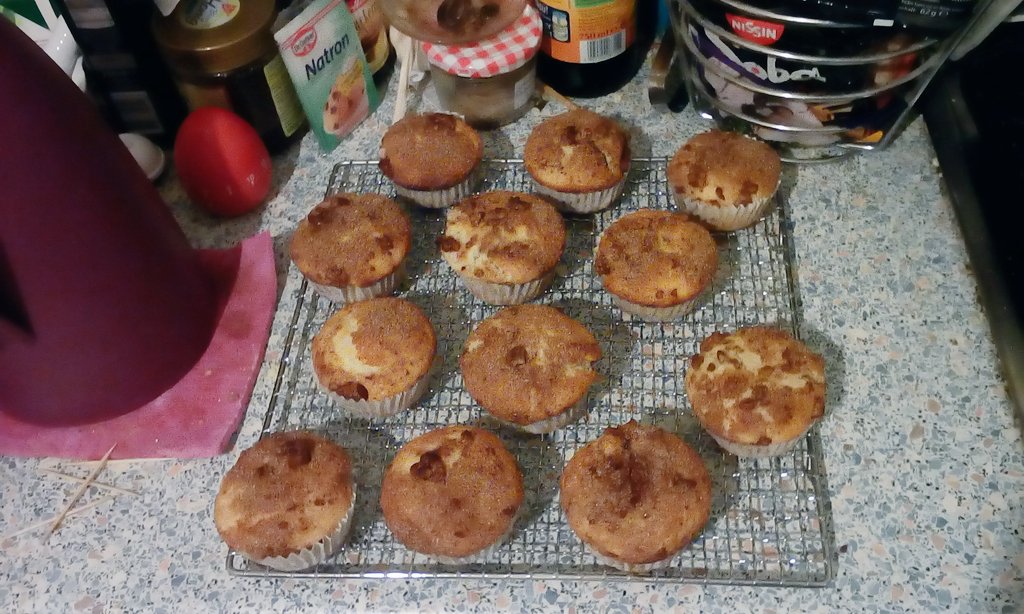 12 muffins, topped with cinnamon sugar and chopped nuts on a cooling rack