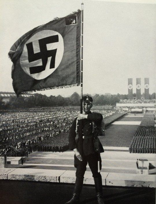 NSDAPHistory's tweet photo. SS member holding a flag at the Nuremberg Rally, 1933. https://t.co/2lXYKJYN8f