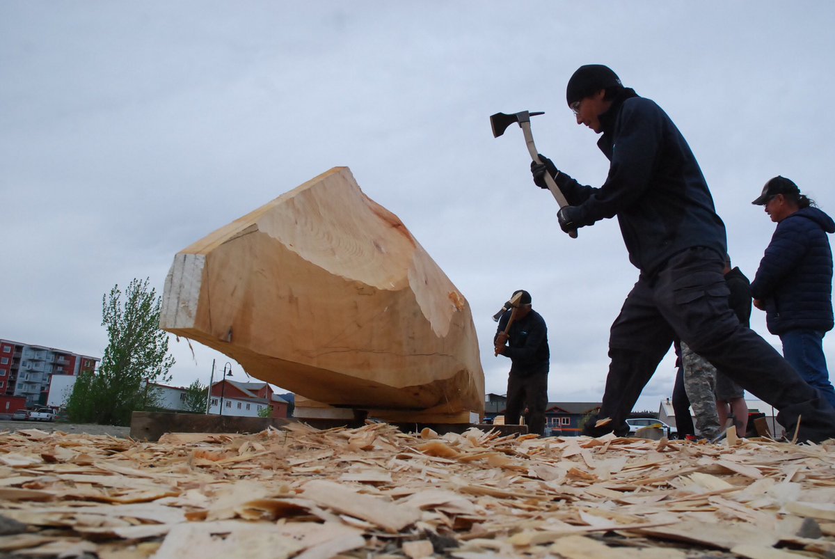 YukonPhilippe's tweet photo. Outside the #MMIWG inquiry today, work continues on a spruce dugout canoe. Master Carver Wayne Price teaches two volunteers to use an adze https://t.co/DIflg5Wltm