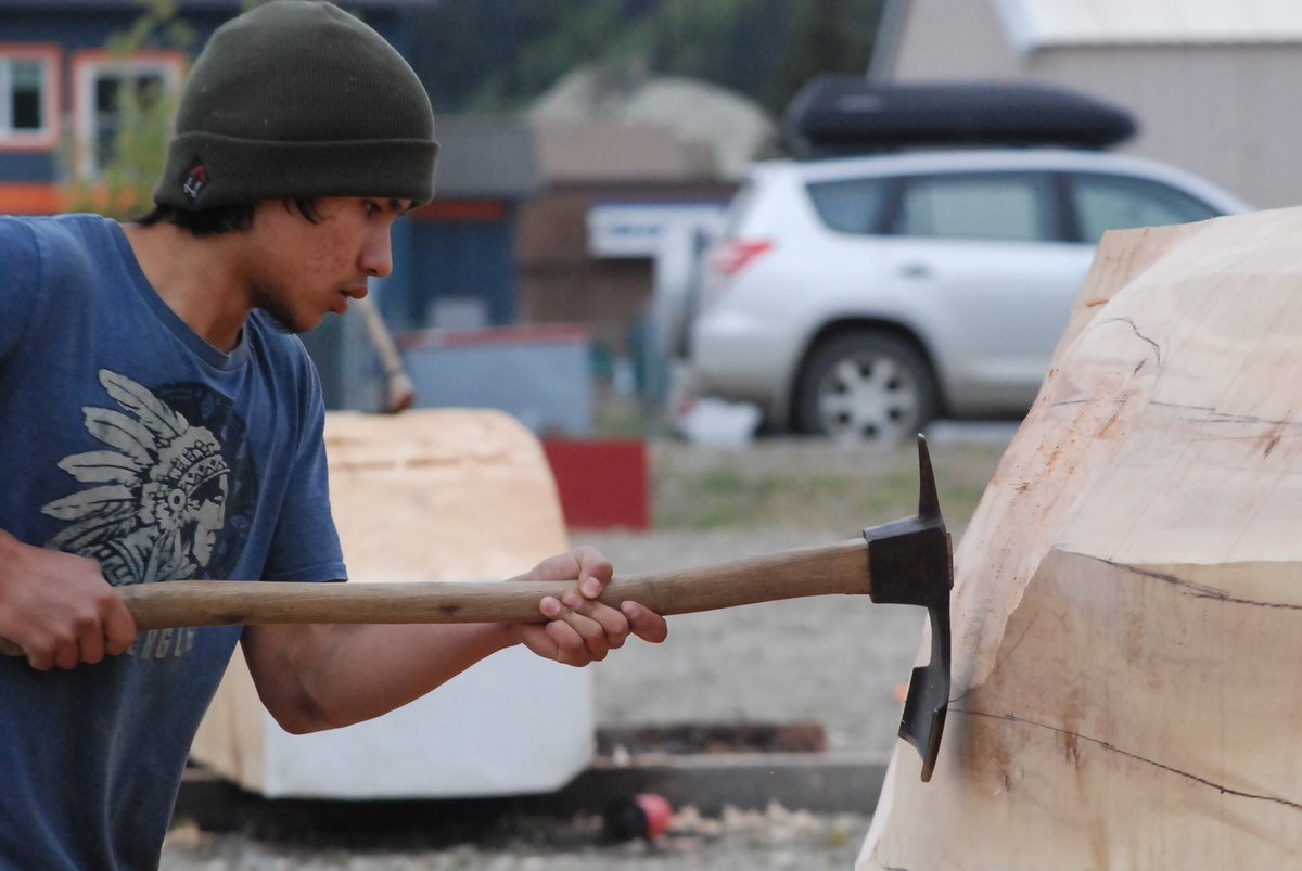 YukonPhilippe's tweet photo. Outside the #MMIWG inquiry today, work continues on a spruce dugout canoe. Master Carver Wayne Price teaches two volunteers to use an adze https://t.co/DIflg5Wltm