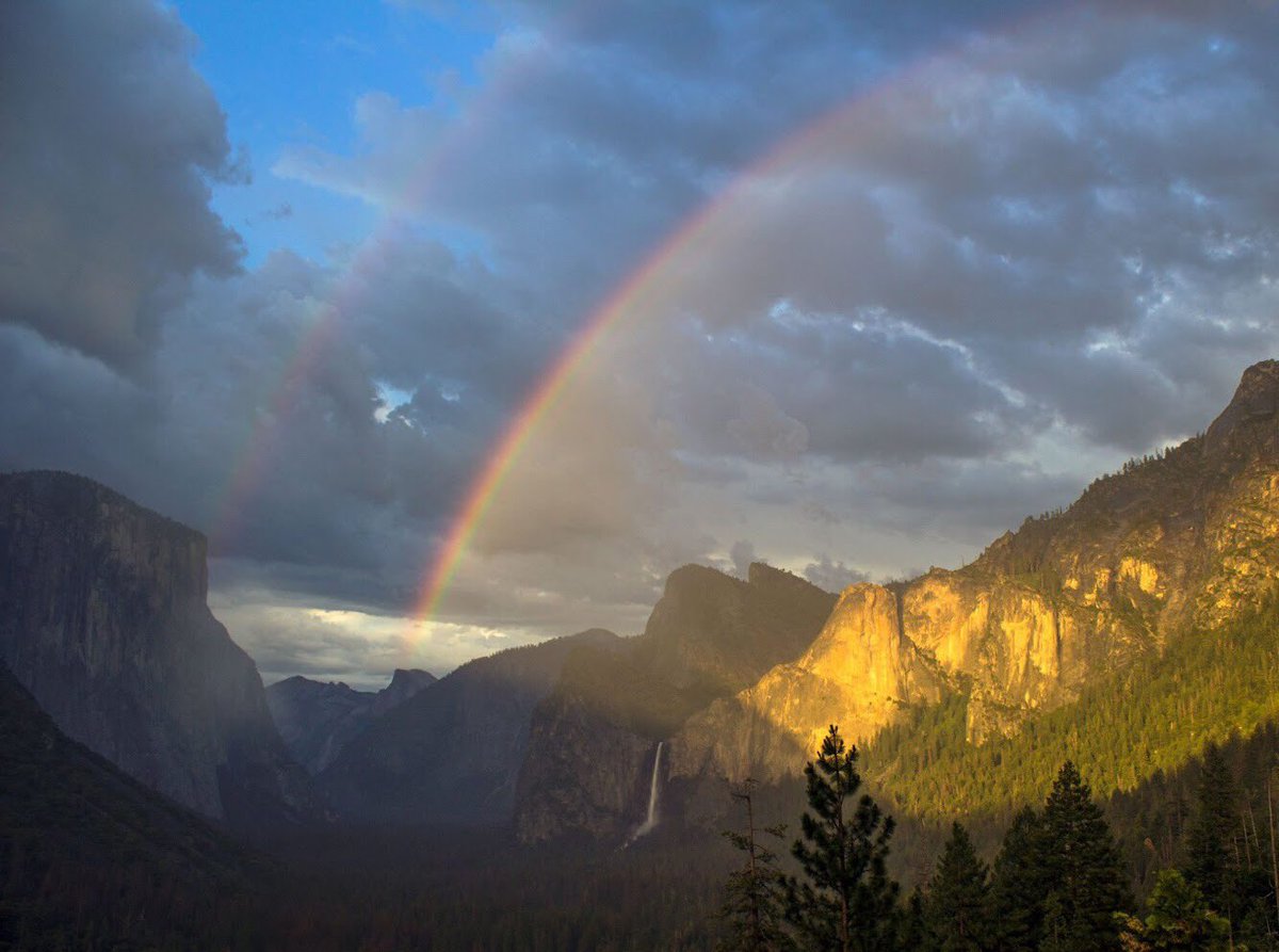 A double rainbow appears over a valley of granite rock formations