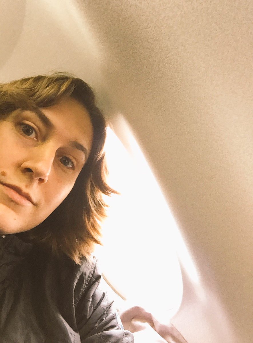 Picture of me leaning into the frame in a pic pointing toward an airplane window and the wall. I'm wearing a black jacket and looking surprised or curious or something. There's a little airplane pillow in the background