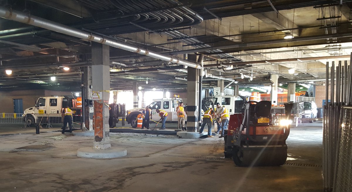 Crews wearing safety vests shovel and rake asphalt in a covered building