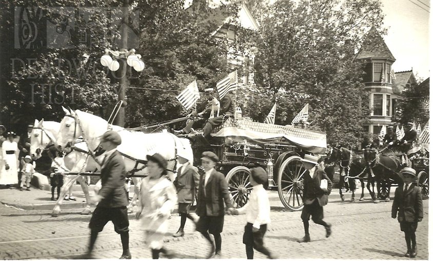 AdamsMuseumHous's tweet photo. White horses pull the Lead Hose Company No. 1 fire wagon in a parade along a street in Lead in the 1900s. @DeadwoodTrust @LeadChamber https://t.co/YbDK4M505E