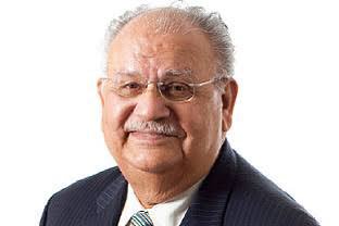 Naresh Chandra studio portrait against white background wearing dark pinstripe suit in 2017.