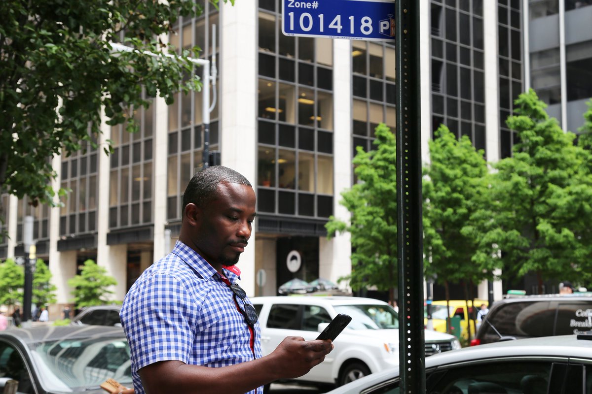 a man looks at his phone while standing on the sidewalk beside parked cars and street signs