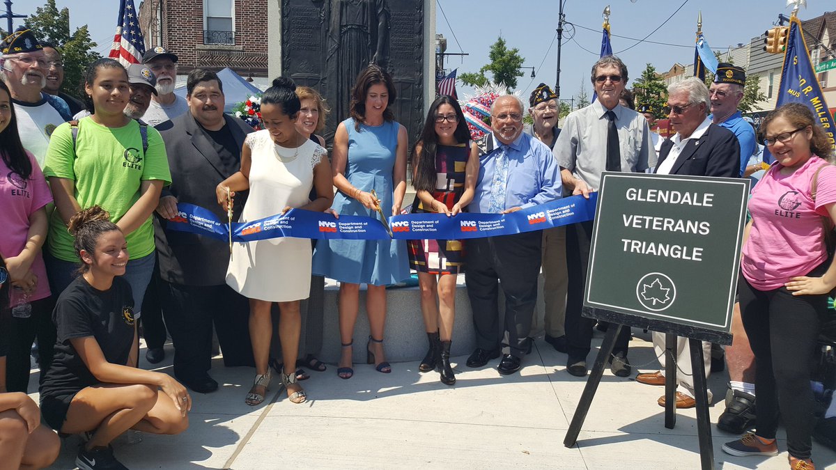 a group of people stand behind a ribbon. a sign says "Glendale Veterans Plaza"