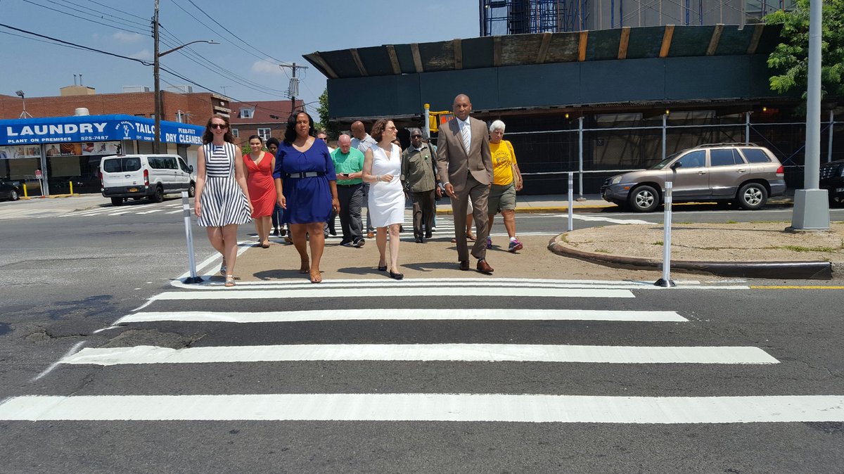 group of people cross the street in a bright white striped crosswalk with a painted center median