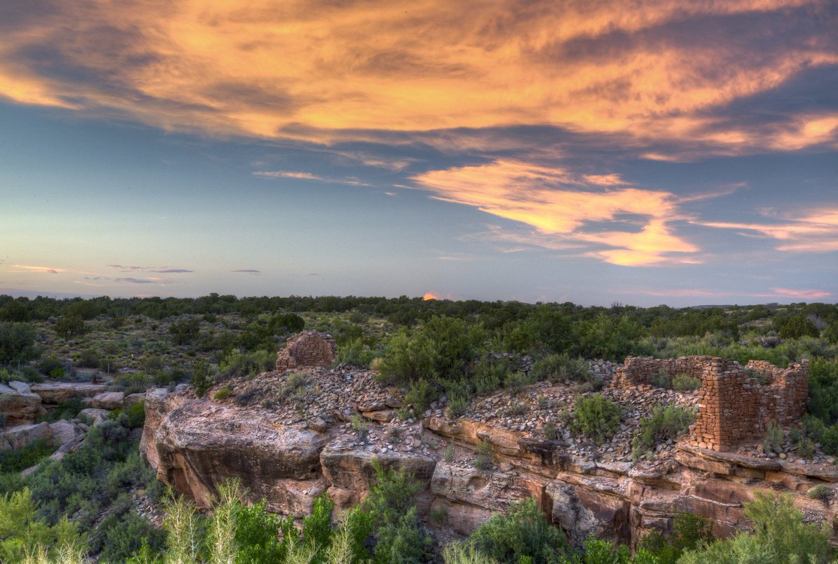 Native American archaeological sites are visible in a green shrub landscape with blue skies and golden clouds overhead