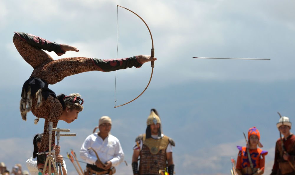 A Kyrgyz woman balances on her hands as she shoots a bow and arrow with her feet during 'Ethno Fest' festival in village of Ton, Kyrgyzstan