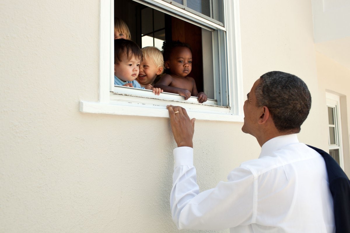 Obama looking up at an open window with babies of various ethnic backgrounds looking out