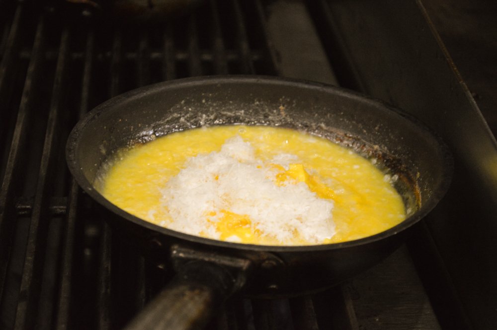 LibraryKitchen's tweet image. Chef Andrea cooks risotto over an open flame before adding a generous portion of cheese to the pan.