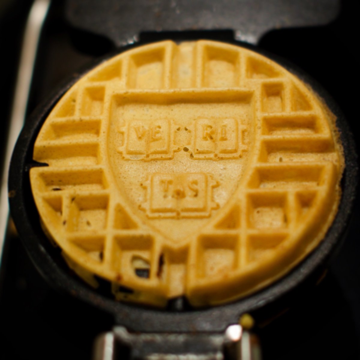 A waffle with the Harvard shield, which bears the motto "Veritas," sitting in a waffle iron.