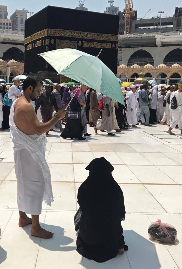 Photos_islam's tweet photo. Un homme protège son épouse du soleil pendant qu'elle accomplit la prière face à la Kaaba https://t.co/LnSo1Aqft2