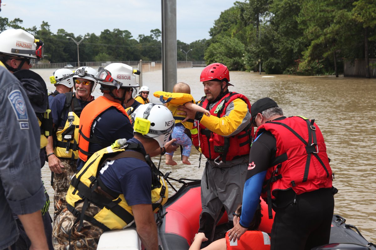 A raft of search and rescue workers in safety gear rescue a small baby from flood waters.