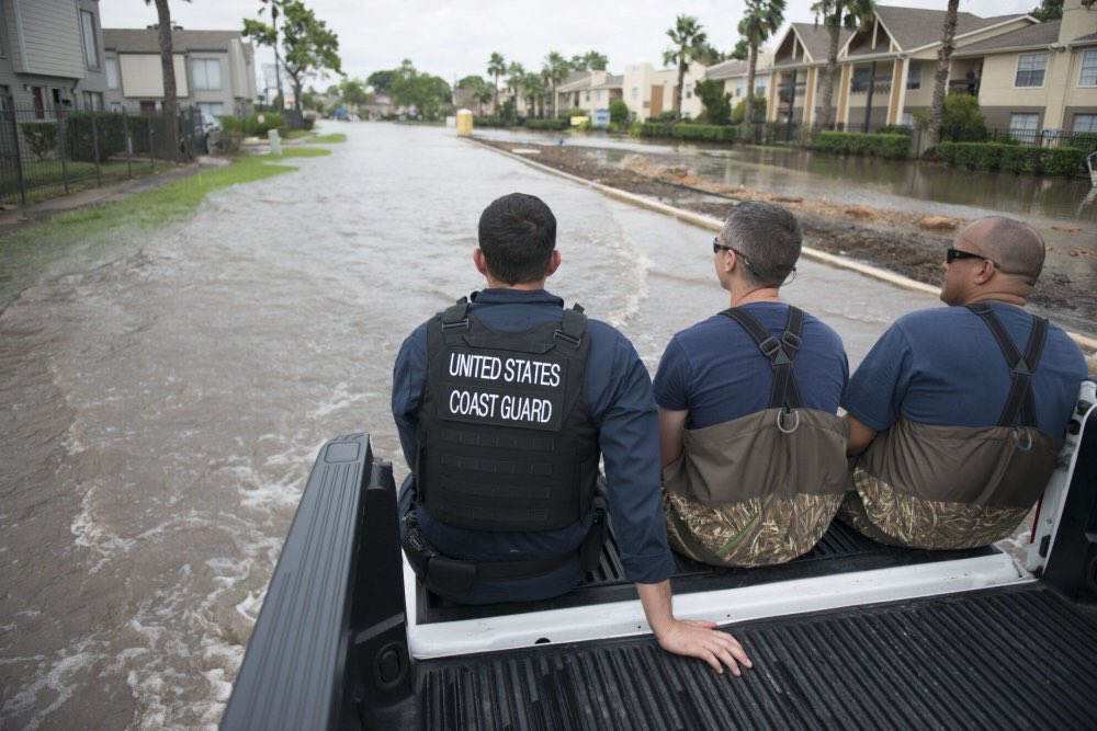 Three Coast Guard rescue personnel sitting on a boat traveling through floodwaters.