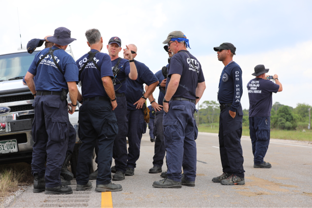 Search and rescue members in dark blue uniforms huddle in a group to prepare for rescues.