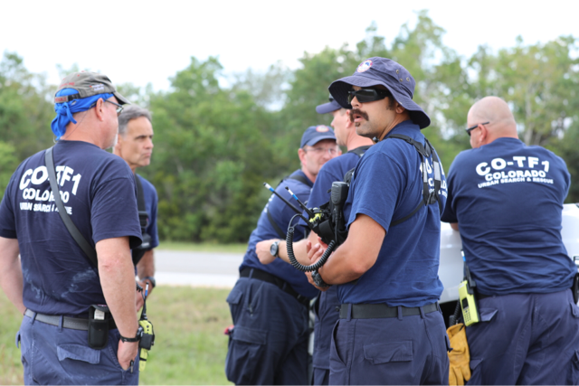 Search and rescue members in dark blue uniforms huddle in a group to prepare for rescues.